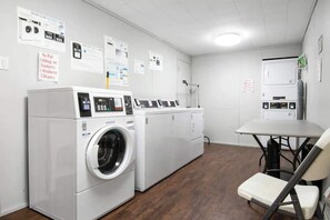 A laundry room with multiple washing machines and dryers, a table with chairs, and informational posters on the walls. - Pet Friendly Cabin in Gatlinburg (Gatlinburg)