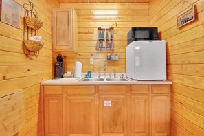 A compact kitchen with wooden cabinets, a white refrigerator, a coffee maker, and a welcome sign. - Pet Friendly Cabin in Gatlinburg (Gatlinburg)