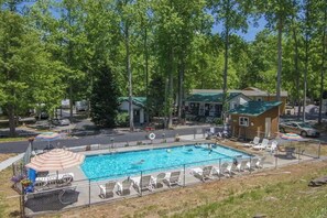 A rectangular swimming pool with lounge chairs and umbrellas, surrounded by trees and a small building. - Pet Friendly Cabin in Gatlinburg (Gatlinburg)