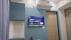 A room with a mounted TV displaying various streaming services, a door with a handle, and an air conditioning unit on the wall. - Hotel Maan Palace (Ahmedabad)