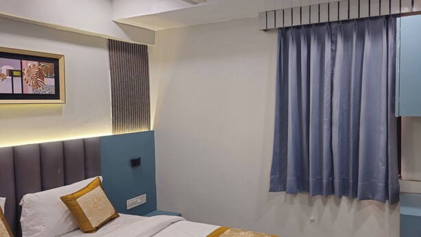 A hotel room with a bed, a wall-mounted TV, a window with curtains, and a framed picture on the wall. - Hotel Maan Palace (Ahmedabad)