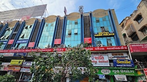 A multi-story building with various signs, including a hotel named 'Hotel Maam Palace' and a pharmacy. - Hotel Maan Palace (Ahmedabad)