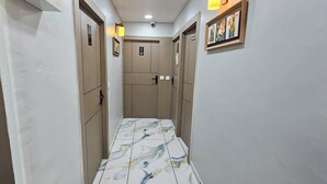A narrow hallway with a patterned floor, doors on either side, and a framed picture on the right wall. - Hotel Maan Palace (Ahmedabad)