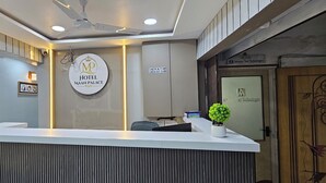A hotel reception desk with a modern design, a ceiling fan, and a sign indicating check-in and check-out times. - Hotel Maan Palace (Ahmedabad)