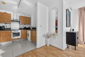 Une cuisine moderne avec des meubles en bois, des appareils électroménagers en acier inoxydable, un lave-linge et un grand miroir.