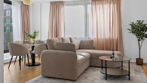 Ein modernes Wohnzimmer mit einem Ecksofa, einem runden Couchtisch sowie einem Essbereich mit Stühlen und einem kleinen Tisch.