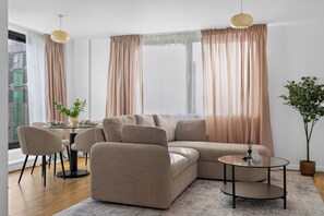 Ein modernes Wohnzimmer mit einem Ecksofa, einem runden Couchtisch sowie einem Essbereich mit Stühlen und einem kleinen Tisch.
