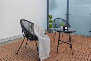 Eine Terrasse mit zwei schwarzen Korbstühlen, einem runden Tisch und einem kleinen Blumentopf.