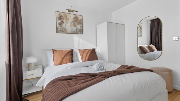 Ein modernes Schlafzimmer mit Bett, Nachttisch, Lampe, Kleiderschrank, Spiegel und Kunstwerk an der Wand.