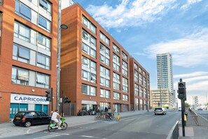 Un immeuble à plusieurs étages avec une façade en briques, une devanture visible avec une enseigne, et une rue où l’on voit des vélos et des voitures.