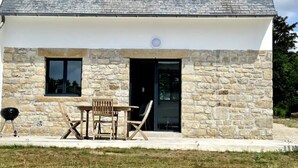 Una casa de pedra amb un teulat inclinat, dues finestres, una porta i una petita zona exterior amb una taula i cadires.