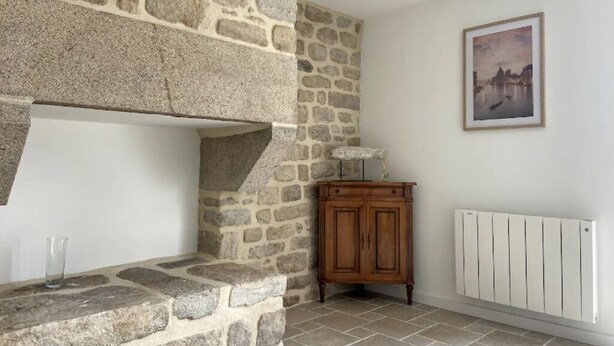 Una llar de pedra, un armari de fusta i un radiador en una habitació amb paret de pedra i un quadre encimbellat.