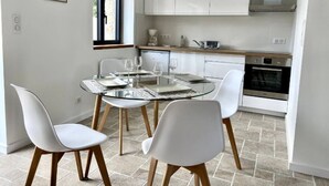 Una cuina moderna amb armaris blancs, forn integrat i zona de dinar amb taula de vidre i cadires blanques.