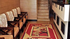 Un hall d’hôtel doté d’un espace recouvert de moquette, de chaises en bois, d’un escalier et d’un comptoir d’accueil.