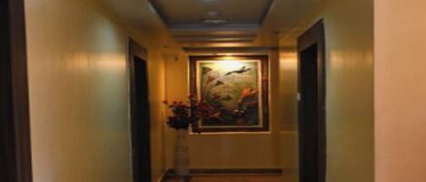 A hotel hallway with a painting on the wall, a vase with flowers, and a carpeted floor.