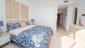 A bedroom with a bed, bedside tables, a dresser, a mirror, and a hallway leading to another room. - Lotus Doña Julia 7.1A (Casares)