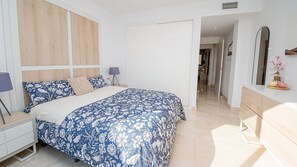 Ein Schlafzimmer mit Bett, Nachttischen, einem Schminktisch und einem Spiegel, sowie einem Flur, der in einen anderen Raum führt.