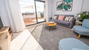 A living room with a grey sofa, a blue armchair, a coffee table, and a view of an outdoor patio with a grill. - Lotus Doña Julia 7.1A (Casares)
