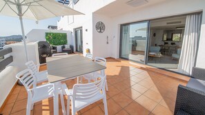 Une terrasse avec une table et des chaises, un barbecue, un canapé et une porte vitrée donnant sur un espace intérieur.
