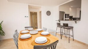 Un coin repas avec une table en bois dressée pour quatre personnes, entourée de chaises, et une cuisine équipée d’appareils électroménagers modernes.