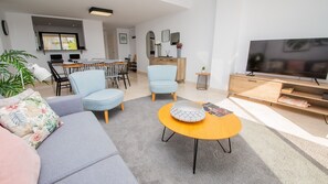 A modern living room with a sofa, chairs, a coffee table, a TV, and a dining area in the background. - Lotus Doña Julia 7.1A (Casares)