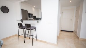 Une cuisine moderne dotée d’un four encastré et d’un four à micro-ondes, de deux tabourets de bar et d’une porte blanche en arrière-plan.
