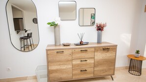 A modern bathroom with a wooden vanity, a large mirror, and a small round table with a potted plant. - Lotus Doña Julia 7.1A (Casares)