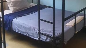 Una camera con letto a castello, una ventola a soffitto, una finestra con tende e un letto con uno zaino.
