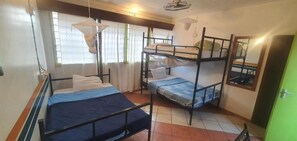 A dormitory room with bunk beds, a window with curtains, a hanging mosquito net, and a green door. - Uhuru Peak Hostel (Moshi)