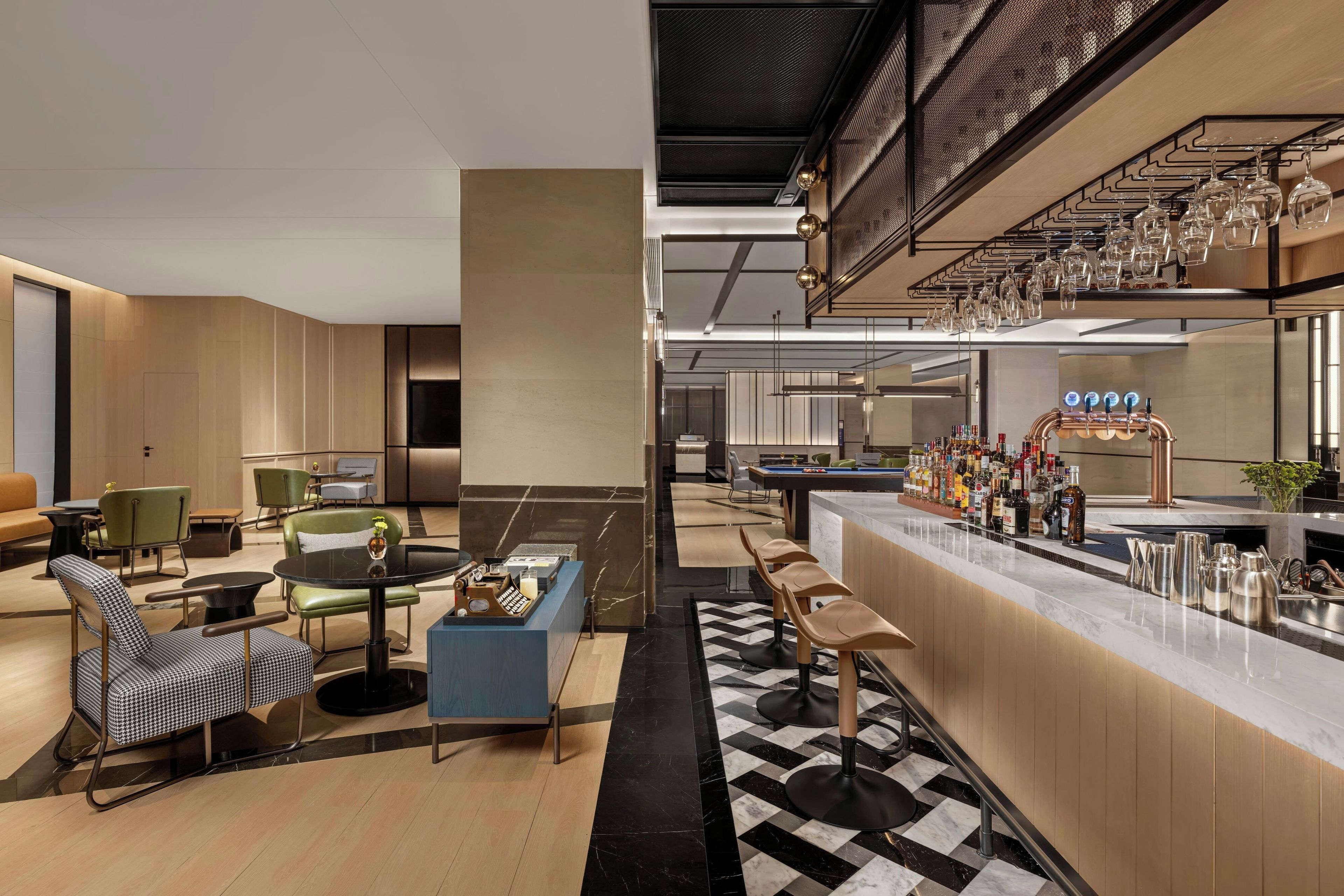 Eine moderne Bar mit Schachbrettmuster-Boden, Barhocker und einer Auswahl an Flaschen.