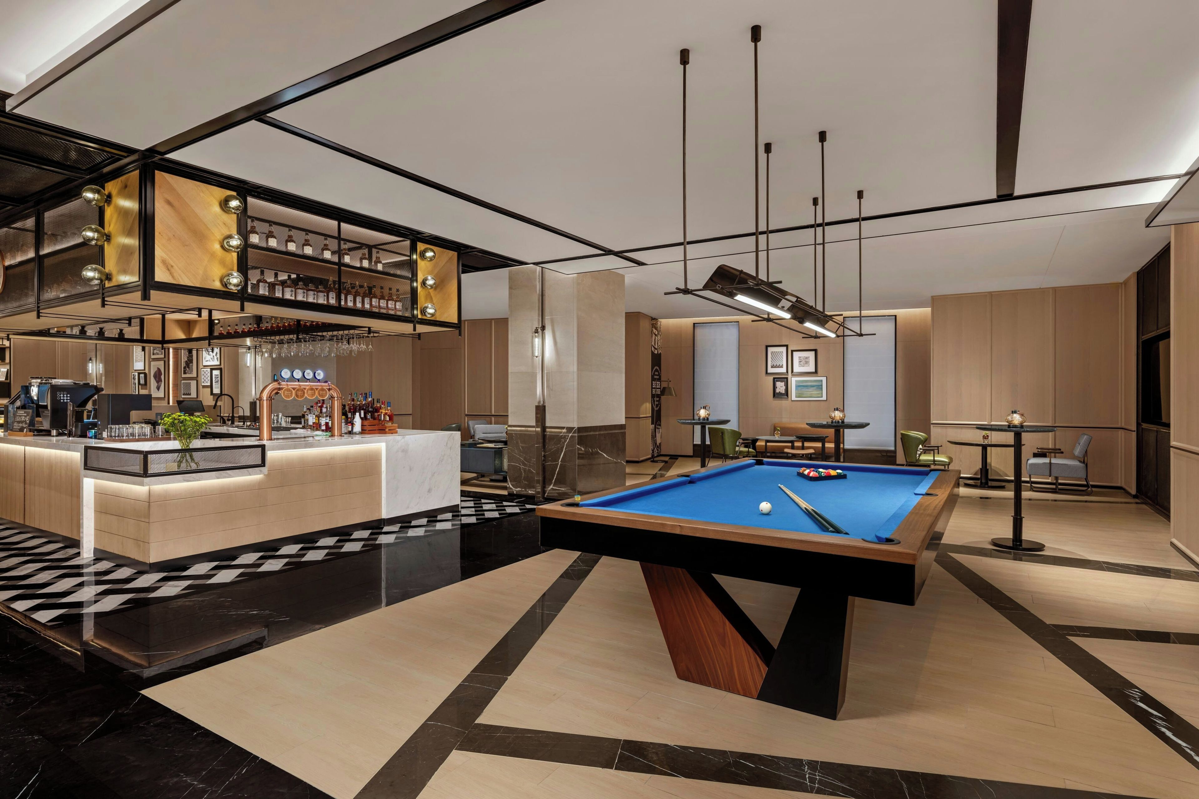 Un espace piscine intérieur moderne, doté d’un bar et de coins salon.