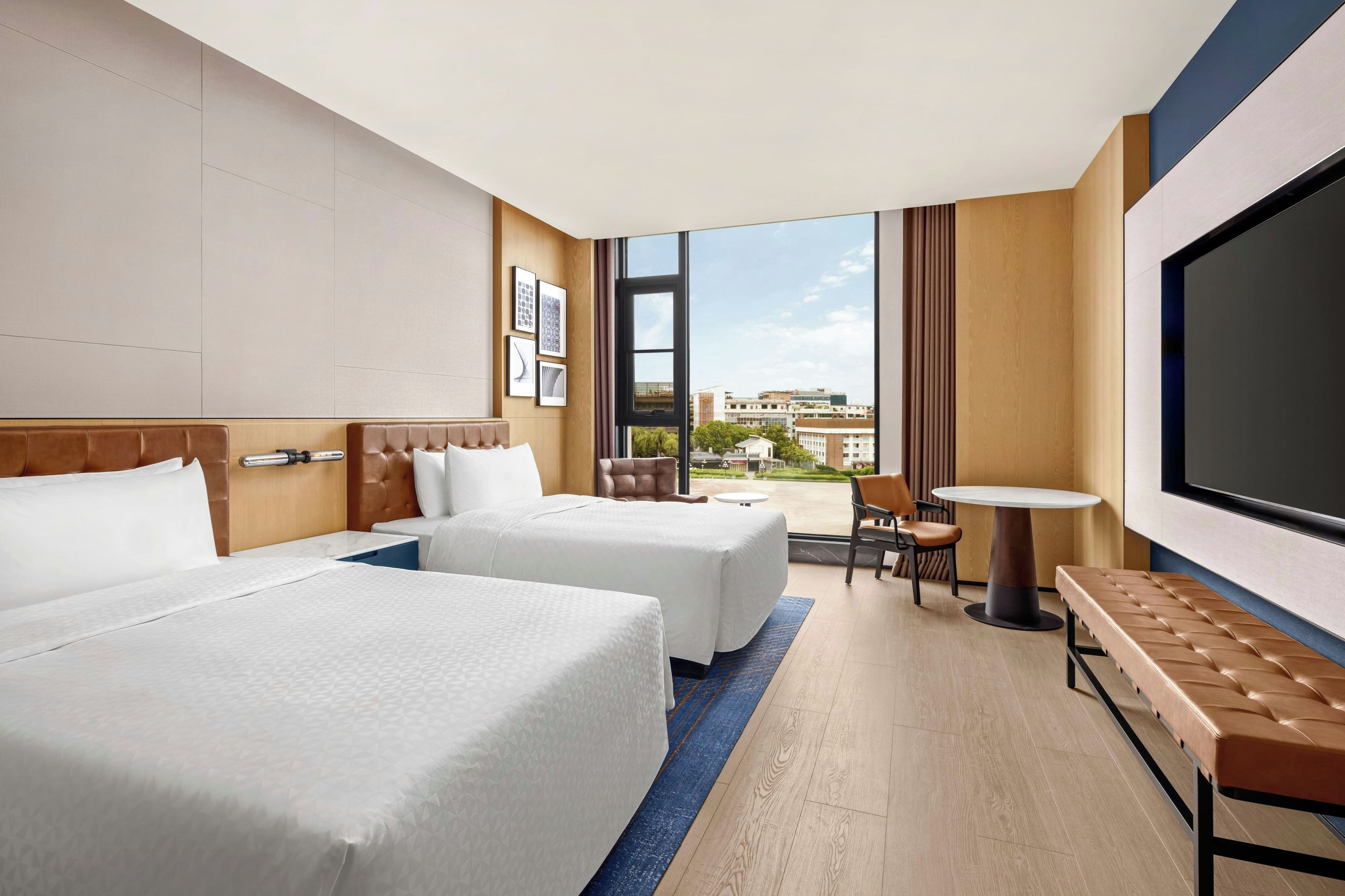 Ein Hotelzimmer mit zwei Betten, einer Sitzecke, einem Fernseher und Blick auf die Stadt.