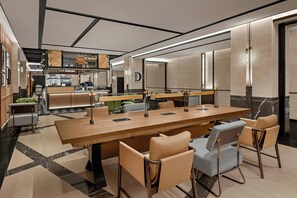 A modern hotel dining area with a long wooden table, leather chairs, and a coffee bar in the background. - Four Points by Sheraton Guilin Central (Guilin)