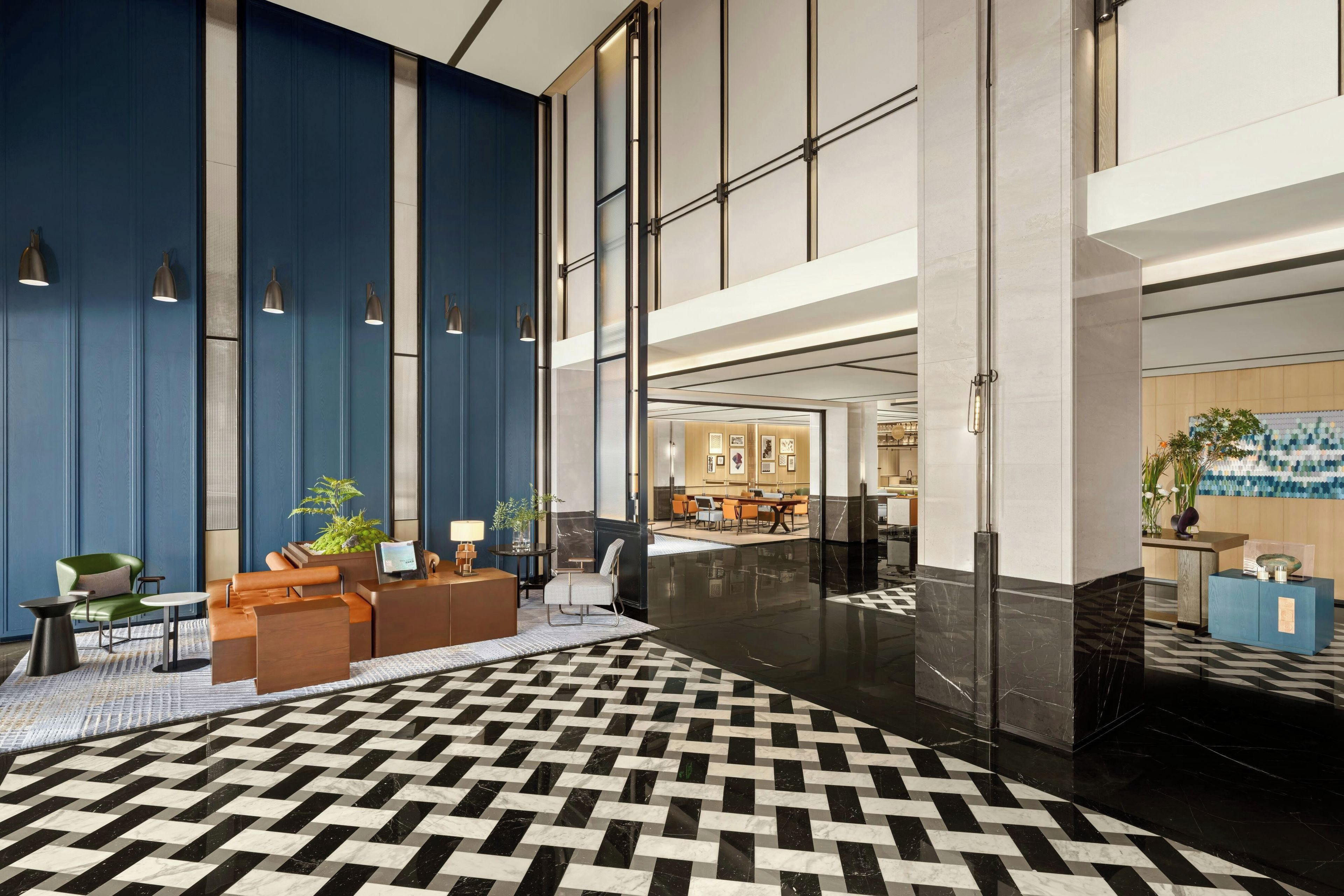 A hotel lobby with a checkered floor, seating area, reception desk, and a view into the dining area.