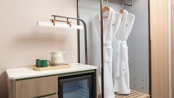 Une salle de bain d’hôtel équipée d’un lavabo, d’un miroir, d’un porte-serviettes avec des peignoirs et d’un petit réfrigérateur.