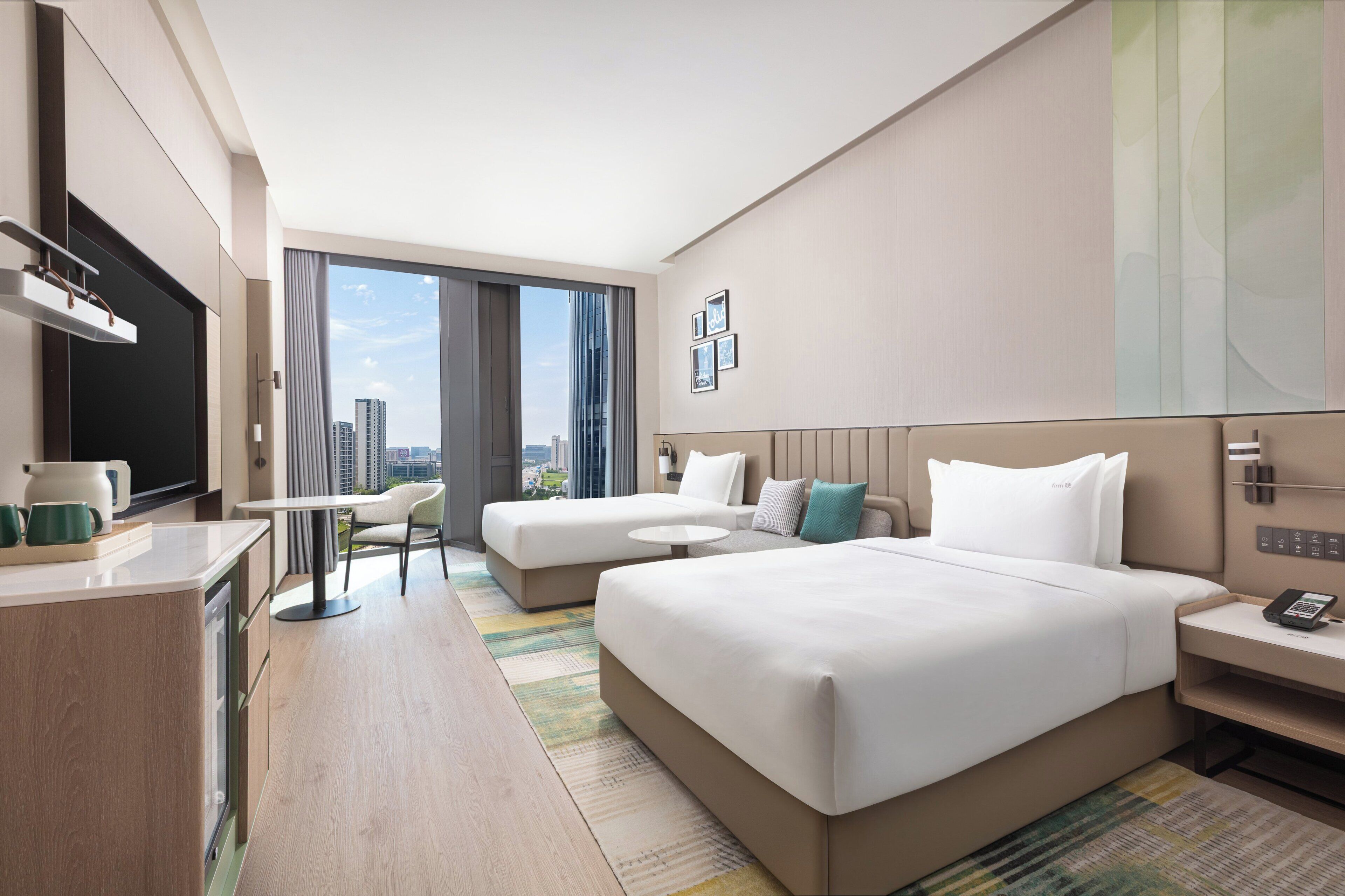 Ein Hotelzimmer mit einem großen Bett, einem Schreibtisch, einem Sessel und Blick auf die Stadt.
