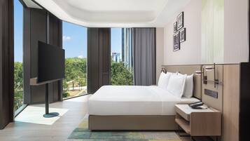 A modern hotel room with a large bed, a flat-screen TV, a bedside table with a remote, and a view of the cityscape.