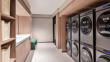 Une buanderie équipée de plusieurs machines à laver et de plusieurs sèche-linge, avec des armoires en bois et un sol carrelé.