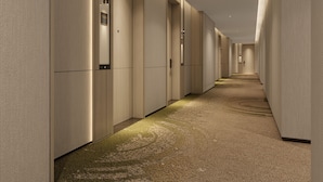 A long, narrow hotel corridor with a carpeted floor and doors on both sides.