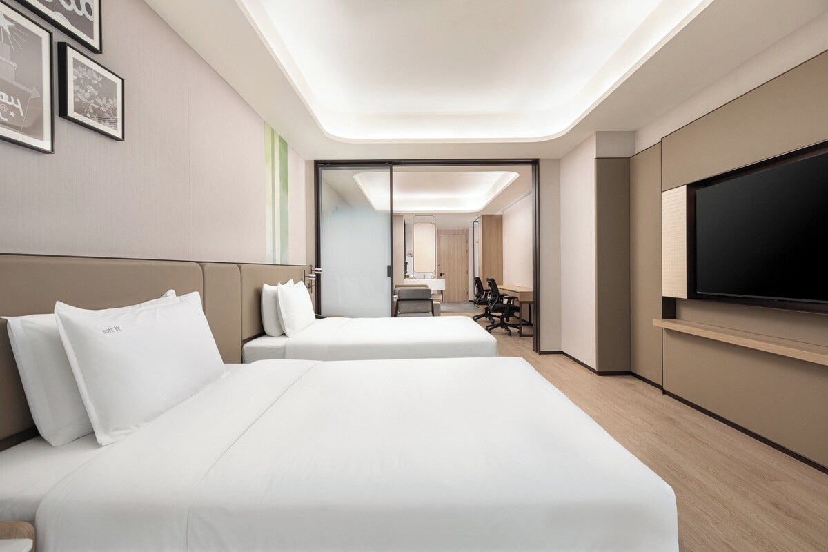 A hotel room with two beds, a TV, and a desk with chairs.