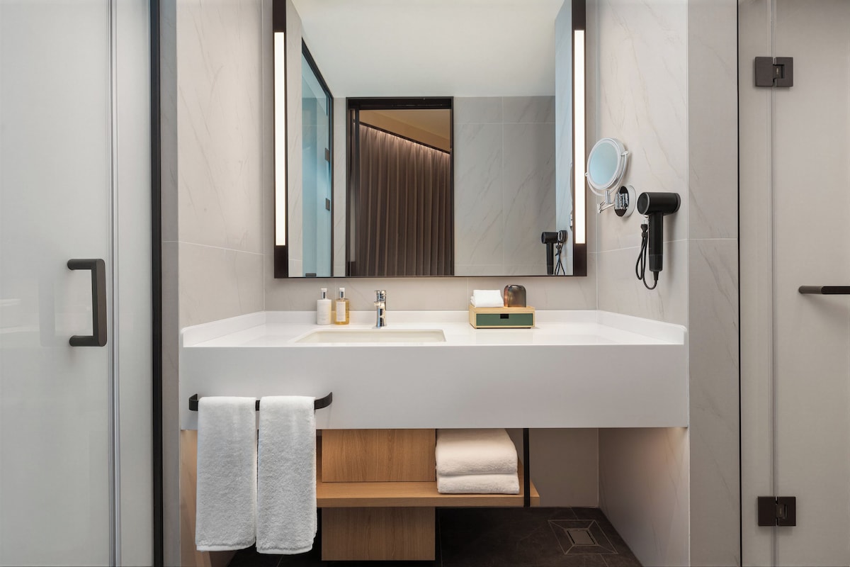 A modern bathroom with a large mirror, a sink, and a towel rack.