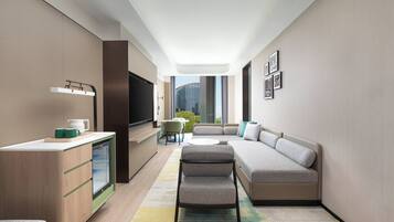 Une chambre d’hôtel moderne dotée d’une kitchenette, d’un coin salon et d’une grande fenêtre donnant sur la ville.