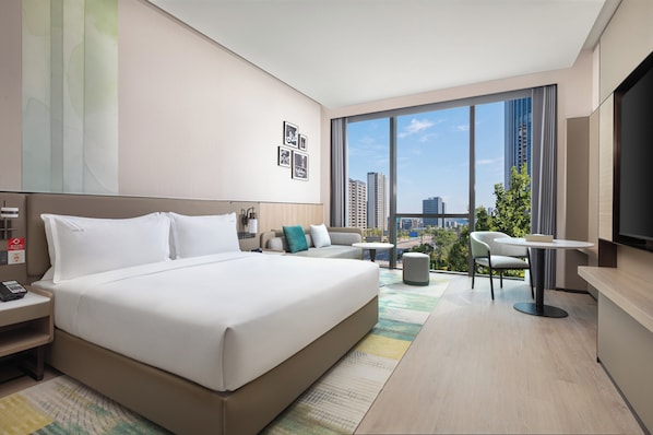 Una habitación de hotel moderna con una cama grande, un sofá, una mesita y un televisor.