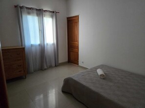 Ein Schlafzimmer mit einem Bett, einem Holzschrank, einer Tür und einem Fenster mit Vorhängen.
