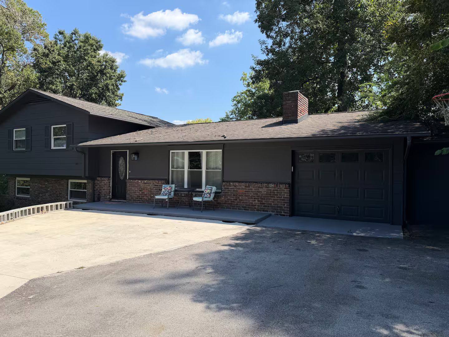 Ein Wohnhaus mit Garage, einer Veranda mit zwei Stühlen und einem Ziegelkamin.
