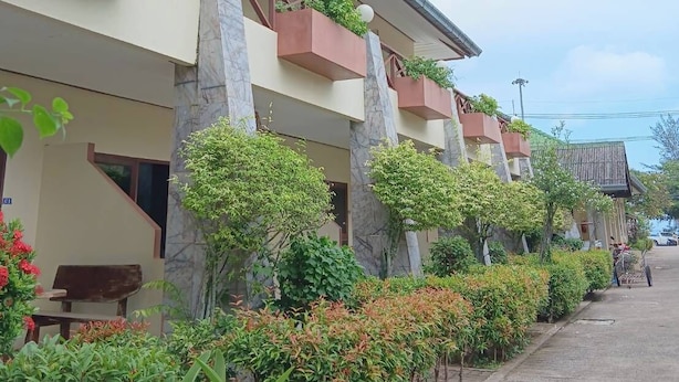 Un hotel con varios balcones, un sendero de concreto y abundante vegetación.