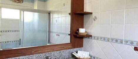 Une salle de bain avec un lavabo doté d’un plan de travail en granit, un miroir, un porte-serviettes et un espace douche.