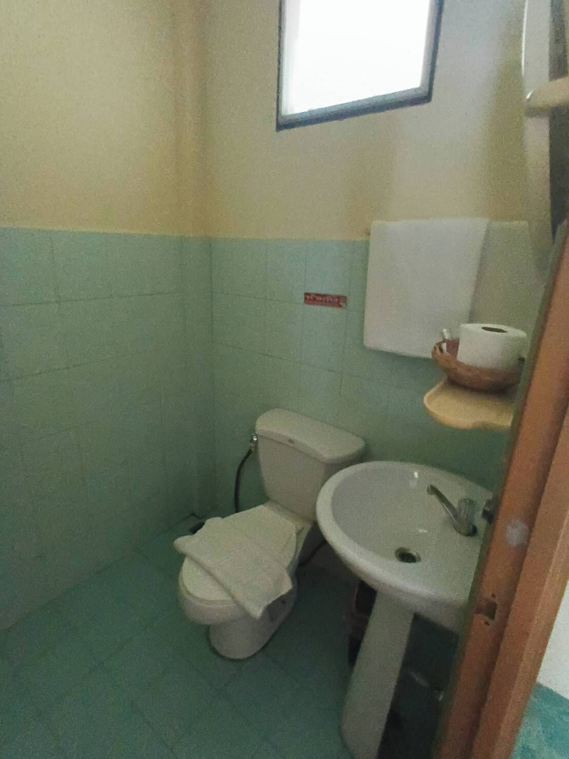 A small bathroom with a toilet, sink, and a window above the sink.