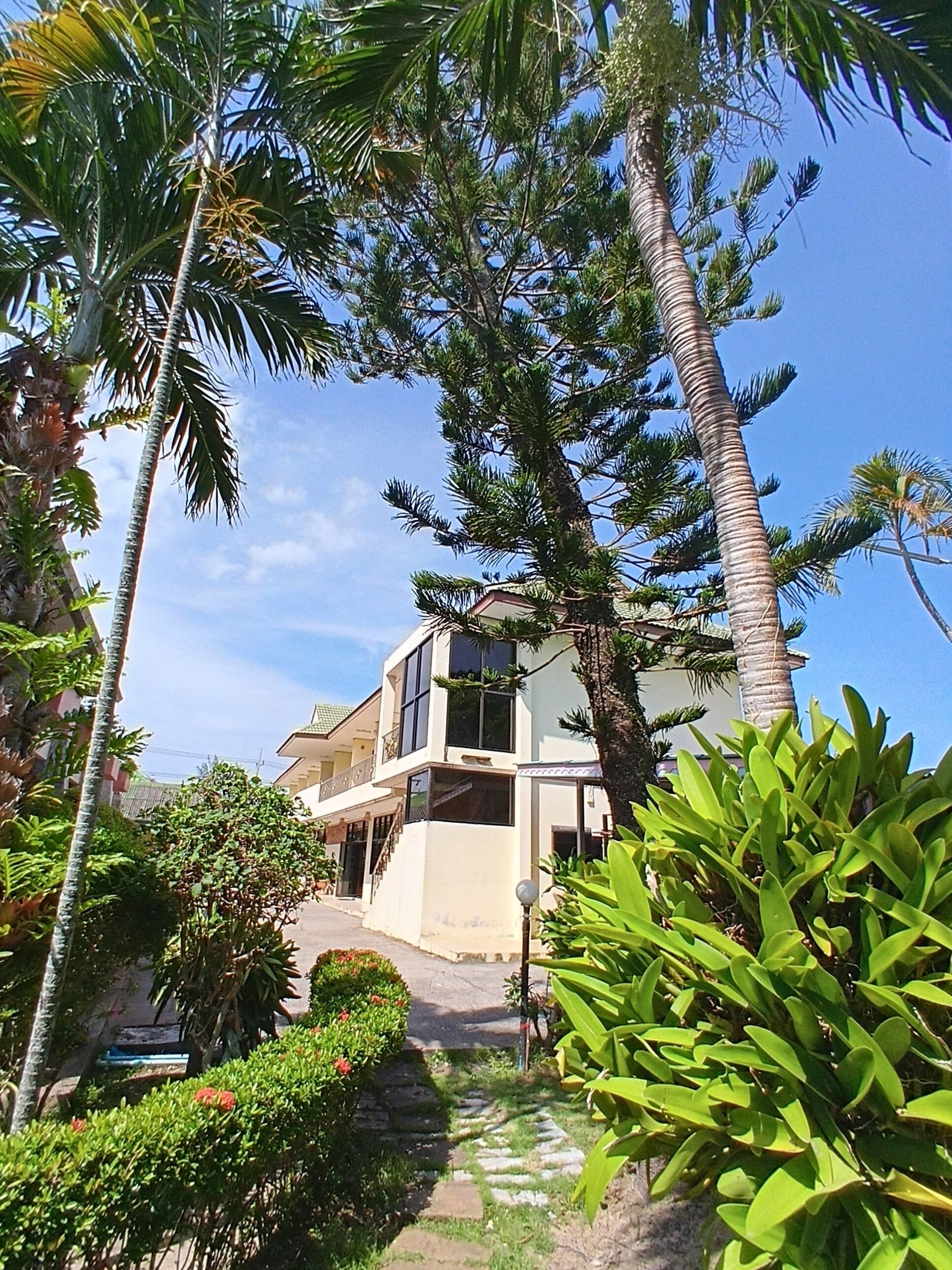 A two-story building with a balcony, surrounded by lush greenery and palm trees.