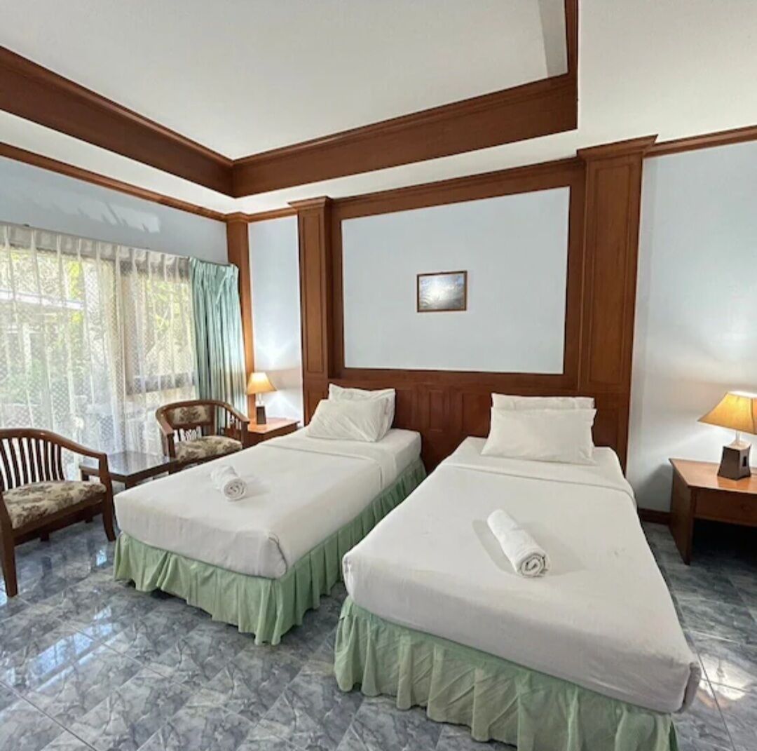 A hotel room with two beds, a chair, a table, and a window with curtains.